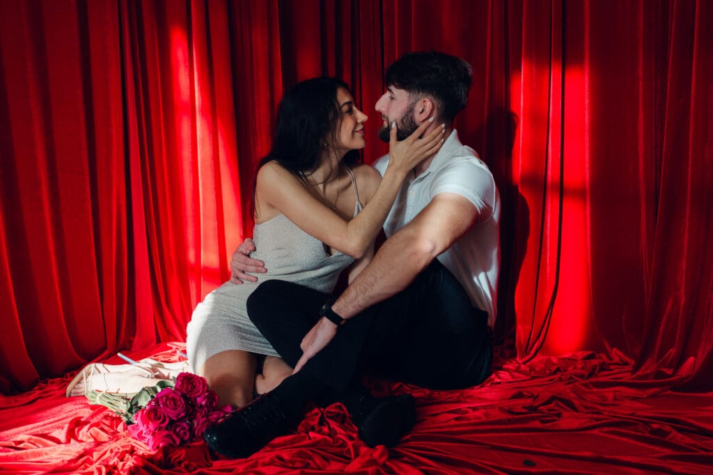 Couple sitting together on red velvet floor with roses during vintage Valentine’s Day photoshoot at LA Loft Studios in Los Angeles.