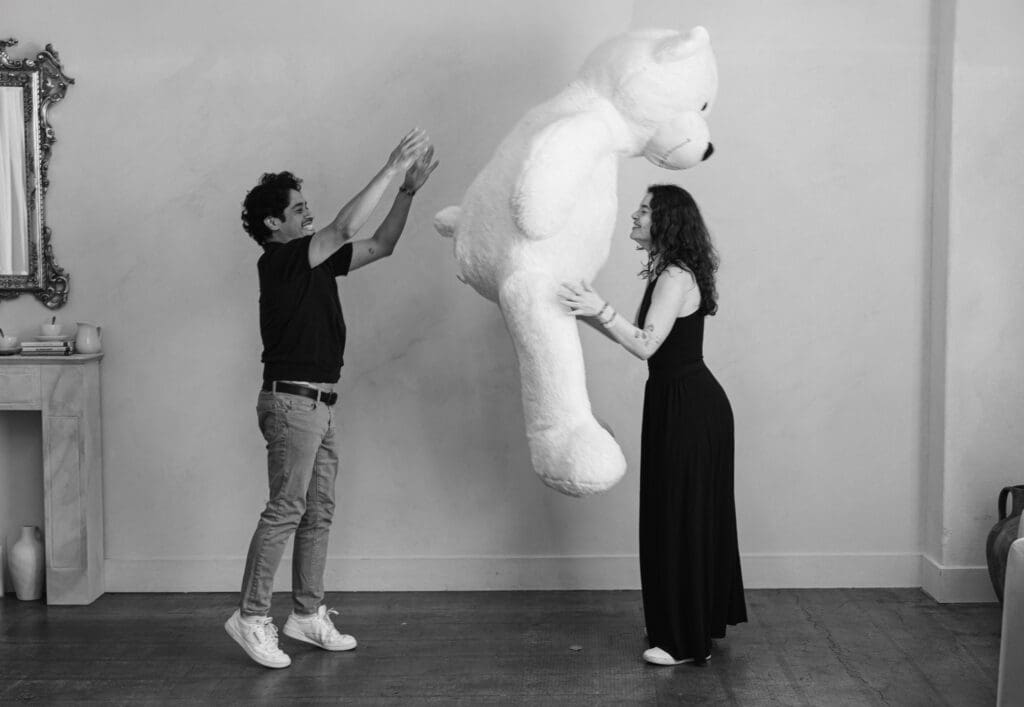Couple playfully tossing oversized teddy bear during Valentine’s Day mini session at LA Loft Studios in Los Angeles, photographed in black and white.