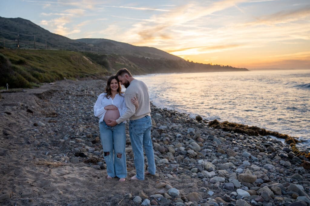 Expectant couple embracing during a sunrise maternity session at Leo Carrillo State Beach in Malibu, California.