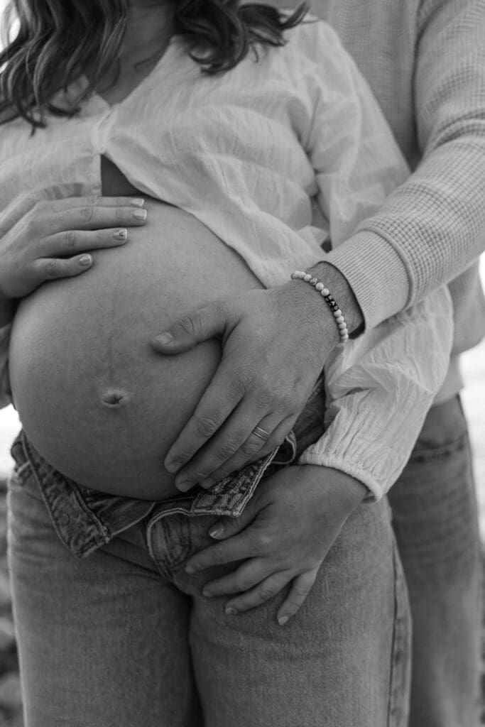Close-up of expectant parents holding their baby bump during an outdoor maternity session in Malibu, California.