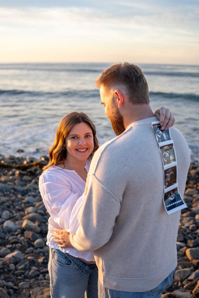 Expectant couple holding ultrasound photos during a sunrise maternity session at Leo Carrillo State Beach.