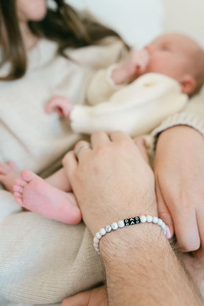 Close-up of a father holding his newborn daughter, featuring a "Dad Dad" bracelet during an in-home lifestyle newborn session.